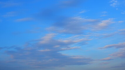 A serene sky with soft, wispy clouds scattered across a blue background. The clouds have a gentle,...