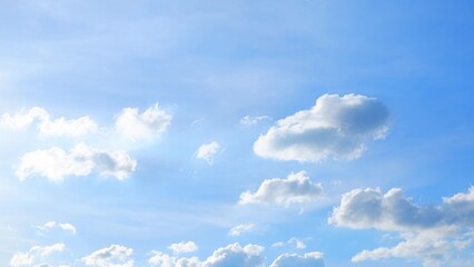 A bright blue sky adorned with scattered, fluffy white clouds. The sunlight enhances the clouds,...