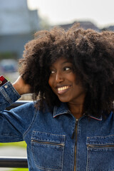 Cheerful woman with curly hair in denim jacket, smiling outdoors, exuding joy and confidence in trendy style