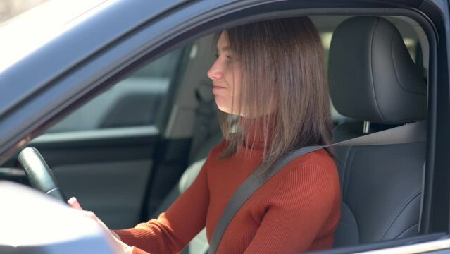 A young woman with brown hair in an orange sweater drives with a frustrated expression, highlighting road rage or traffic-related stress