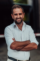 A successful businessman in a white shirt with crossed arms posing outdoors