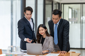 Business team collaborating on a project. Two men and a woman are discussing plans in a modern office environment with a laptop.