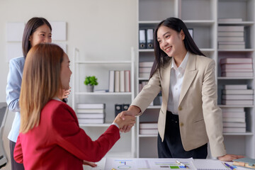 Businesswomen shaking hands in an office meeting, signifying a successful business agreement....