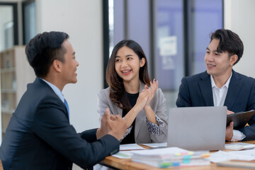 Team of three business professionals collaborating cheerfully during a meeting, discussing...