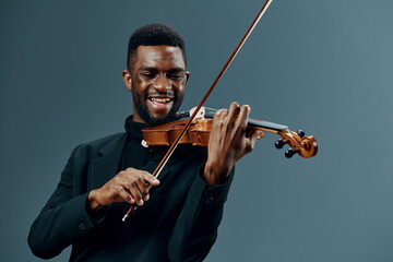 Talented young African American man playing the violin on a neutral gray background in a music and...