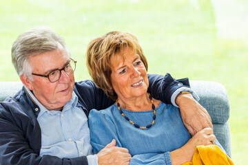 A heartwarming image of an elderly couple sitting closely together on a couch, both smiling and...