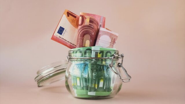 Stop motion of Euro cash banknote come to saving money in glass jar on beige background. Consumption and economy Collecting money. Tips. Extra money, passive. Copy space