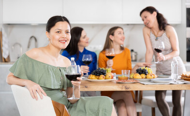 Asian woman drinking wine in company of friends at home party in kitchen