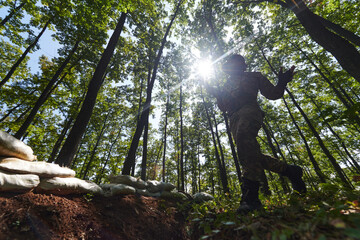 An elite soldier adeptly clears military barriers in the perilous wooded terrain, showcasing...