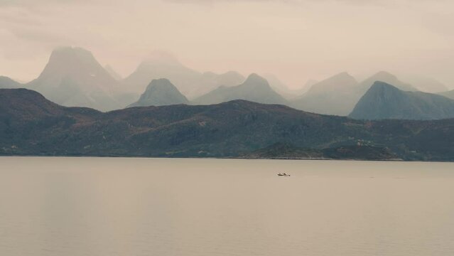 Layers of mountain ranges wrapped in thick fog tower above the calm fjord.