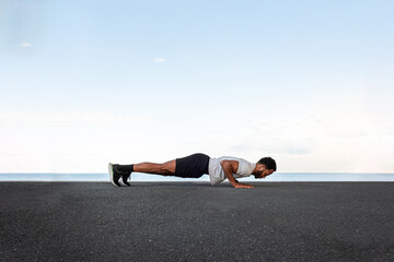 Side view of young African American male wearing sportswear doing push ups outdoors. Copy space.