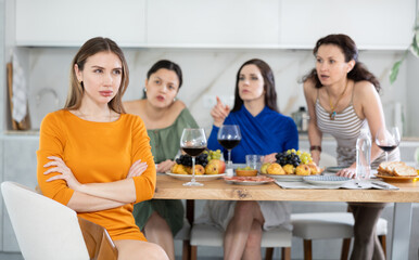 Woman looking hurt and upset during argument with female friends sitting at table in background...
