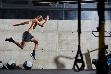 A muscular man captured in air as he jumps in a modern gym, showcasing his athleticism, power, and...