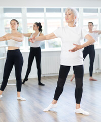 In dance studio, mature woman in group lesson with students rehearses, practices ballet dance, staging.