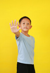 Portrait of Asian boy child show stop sign gesture isolated on yellow background. Focus at his face.