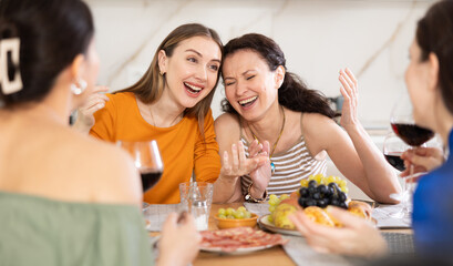 Girlfriends chatting and drinking wine at home party table in kitchen