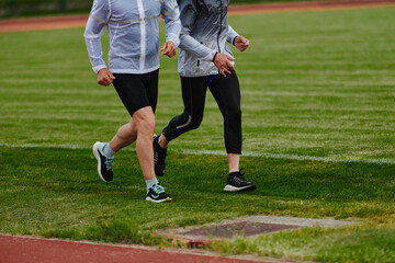 Fototapeta premium An inspiring and active elderly couple showcase their dedication to fitness as they running together on a lush green field, captured in a close-up shot of their legs in motion.