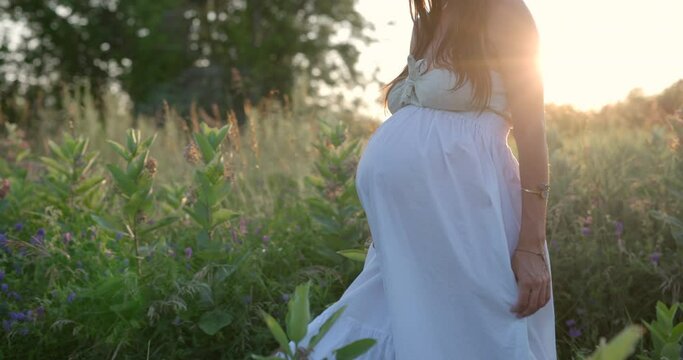 Woman nearing end of pregnancy walks through flower field at sunset - side profile focus on belly