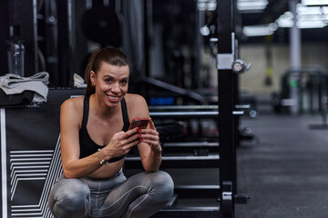 A fit woman in the gym taking a break from her training and uses her smartphone, embracing the convenience of technology to stay connected