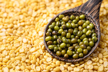 Green mung bean seed in spoon with yellow peeled split mung bean background, Food ingredient
