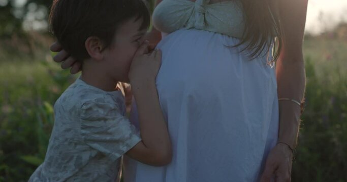 Young boy whispers to mother's pregnant belly in field