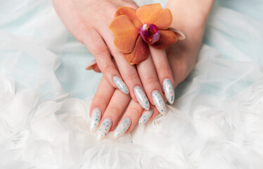 Showcasing Floral Nail Art and Holding an Orange Blossom on a Soft Textured Surface