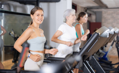 Fototapeta premium Young woman in sportswear training on treadmill in gym