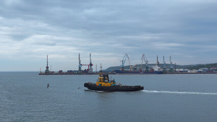 Fishing boat on background of port in cloudy weather. Clip. Fishing vessel sails out of seaport into sea. Fishing boat sails into sea on cloudy day