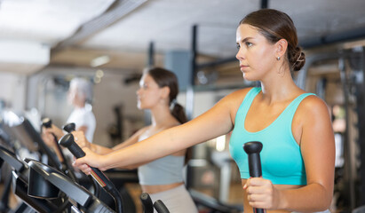 Young athletic woman working out on elliptical machine in gym