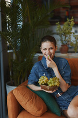 Woman sitting on a couch with a bowl of grapes in front of her, relaxing at home concept