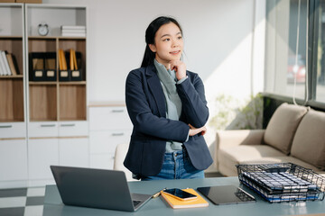 Asian woman sitting at a desk using a laptop computer Navigating Finance and Marketing with...