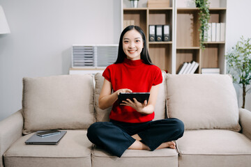 Obraz premium Young asian woman relax on comfortable couch at home texting messaging on smartphone and tablet smiling