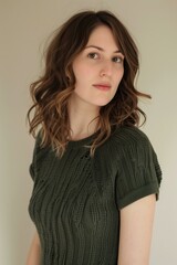 Obraz premium Caucasian woman standing, wearing a green short-sleeve knit dress, with shoulder-length wavy brown hair, beige background