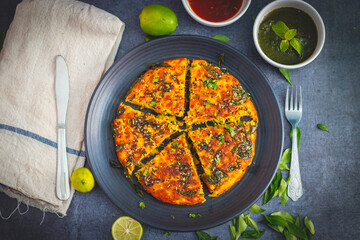 selective focus of Gujrati dish handvo slice tringle cut decorated with lemon, curry leaves, mint chutney and tomato sauce.