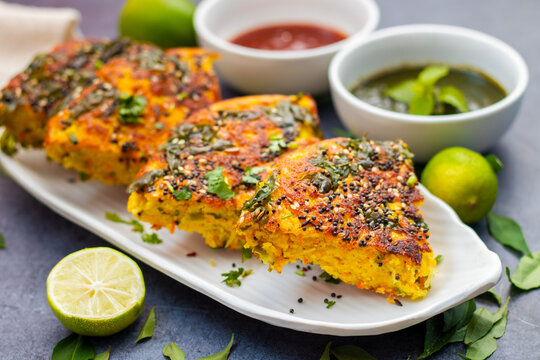 selective focus of Gujrati dish handvo slice tringle cut decorated with lemon, curry leaves, mint chutney and tomato sauce.