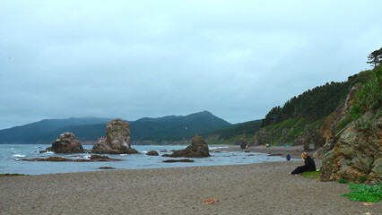 People relax on rocky coast with mountains on cloudy day. Clip. Beautiful coast with rocks and...