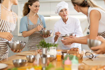 Elderly woman cook at master class teaches group of woman how to cook food
