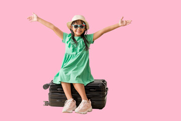 Happy smiling asian little girl were hat and sunglasses posing with sitting on a suitcase,...