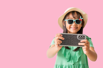 Happy smiling asian little girl were hat and sunglasses poses with using smart phone, exuding...