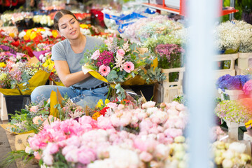 Smiling young woman customer choosing bouquet of flowers in open-air plants market