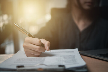 Woman hand holding a pen to sign a document or approval agreement contract on the desk.