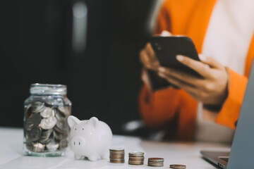 Beautiful Asian businesswoman insert coins in a pin piggy bank on the table. saving money,...