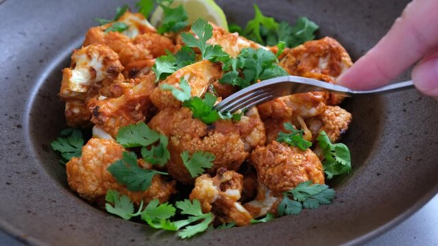 Baked cauliflower in tomato sauce with herbs, white background.