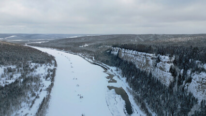 Winter forest landscape and pine tree forest growing on cliff over frozen river in snow. Clip. Breathtaking aerial view of natural landscape.