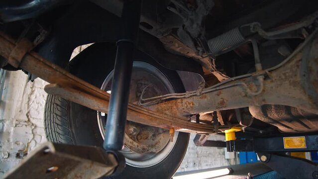 Undercarriage view of a car on a lift, showing a wheel and rusty suspension system during maintenance in a workshop.