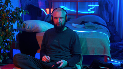 A guy in a neon room listening to music alone and relaxing. Media. Room of a teenager and mess.