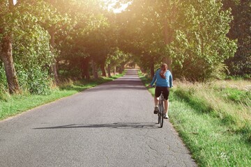 Fototapeta premium Young woman cycling in open fields. Travel by bike.