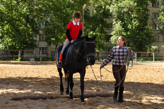 Instructor guides young rider over obstacle during training.