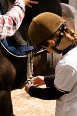 Young rider securing saddle straps on horse.