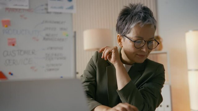 Smiling middle-aged businesswoman works on laptop in office, loves her job